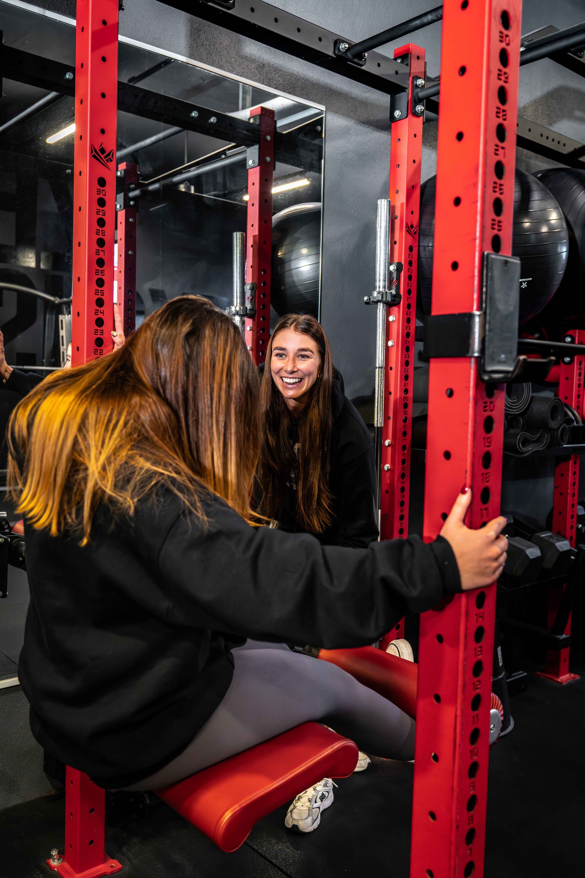 Trainerin coacht Mitglied bei Squat-Übung am Rack