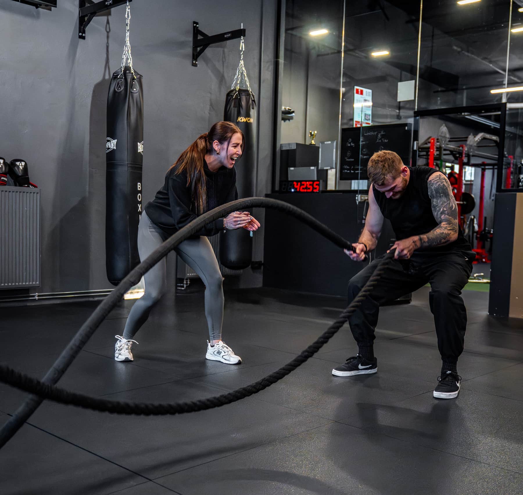 Personal Trainer im Fusion Fit Club feuert eine Kundin beim Battle-Ropes-Training an
